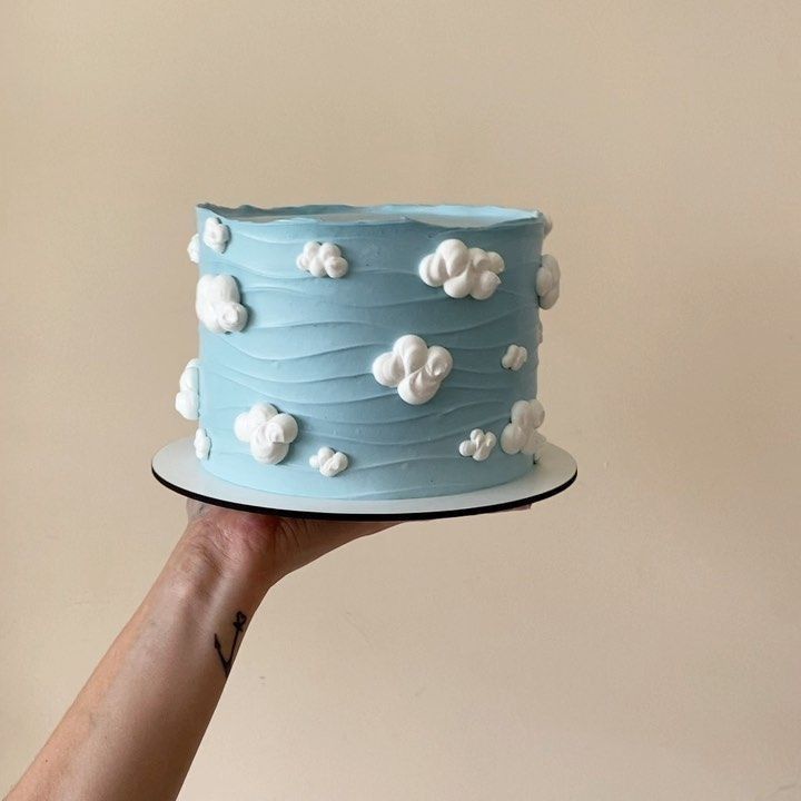 a hand holding a blue cake with white clouds on it