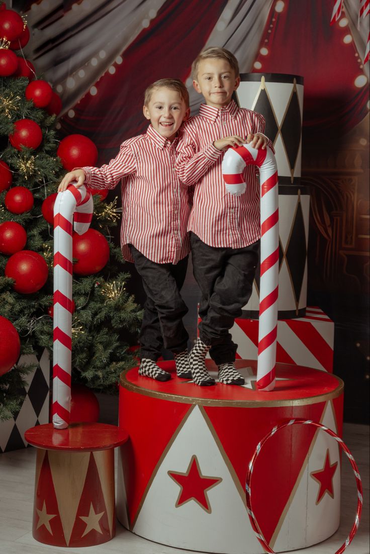 two young boys standing next to each other in front of a christmas tree with candy canes