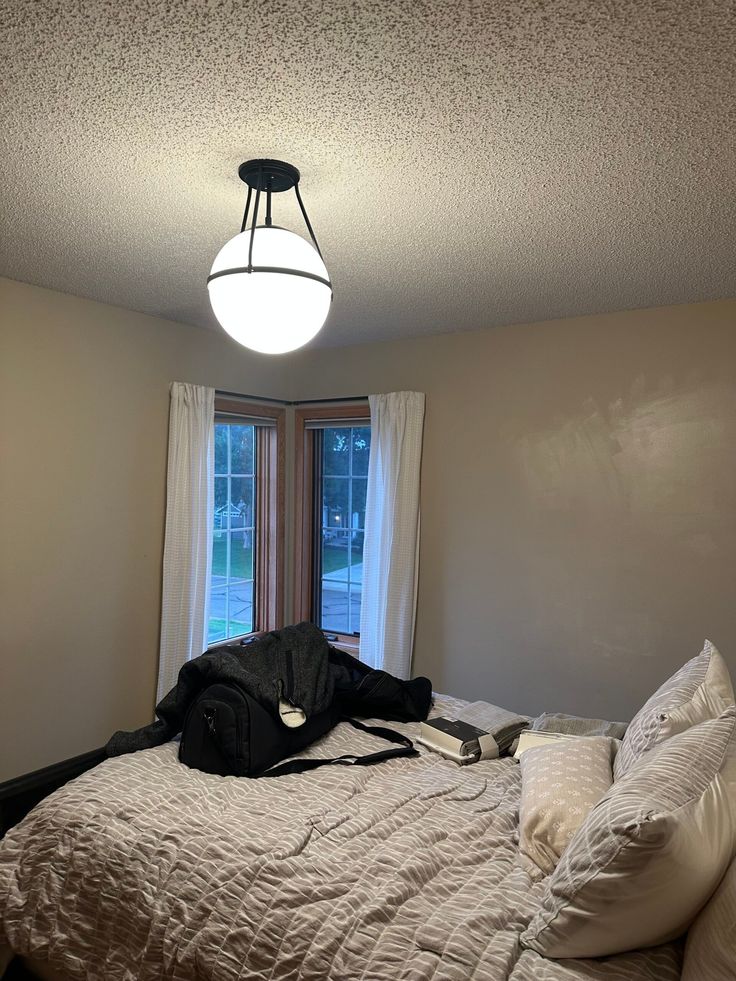 an unmade bed sitting in a bedroom next to a window with a light on