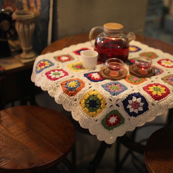 a crocheted tablecloth with tea pot and cups on it sitting on two wooden chairs