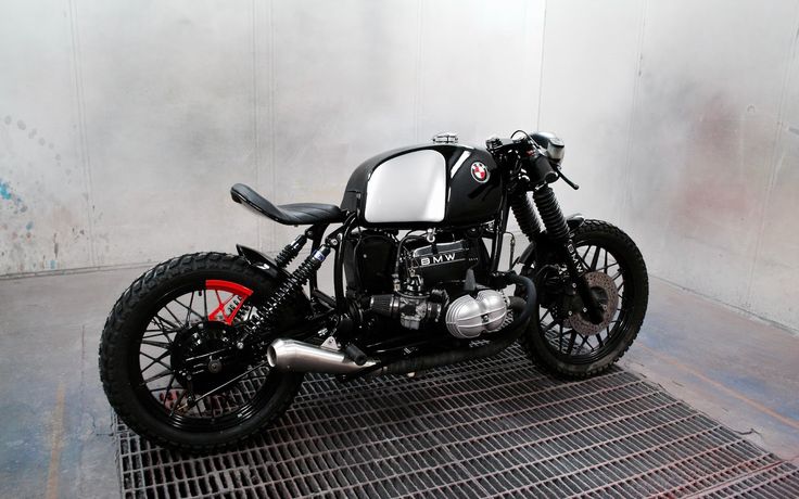 a black and white motorcycle parked on top of a metal grate covered floor next to a wall