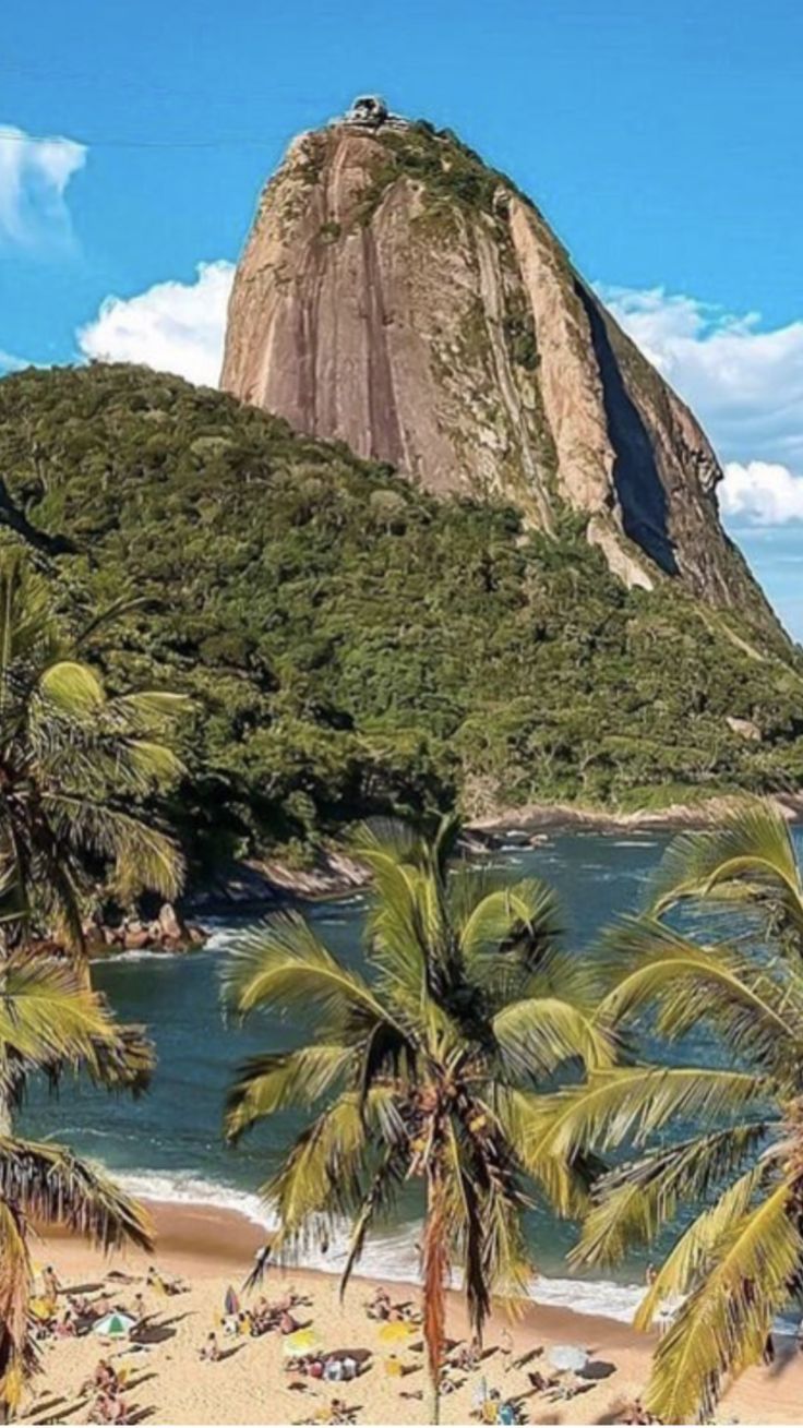 the beach is lined with palm trees and people on it's sides, near a mountain