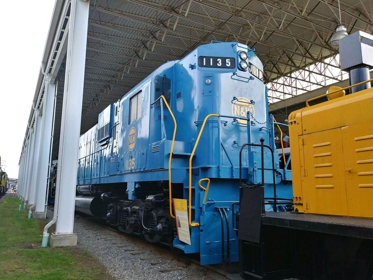 a blue and yellow train sitting on the tracks at a train station under a roof