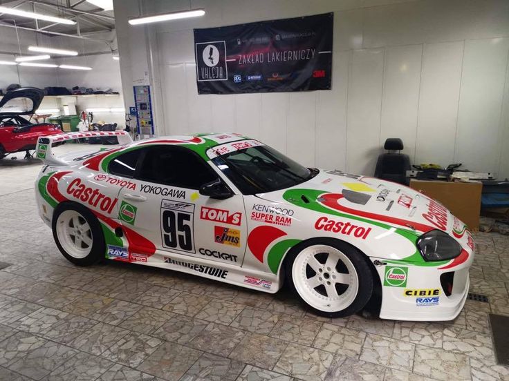 a white car with red, green and yellow paint on it's side in a garage