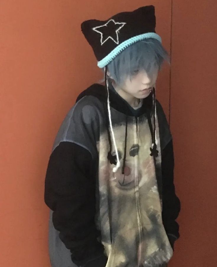 a young man with blue hair wearing a black and grey hoodie standing in front of an orange wall