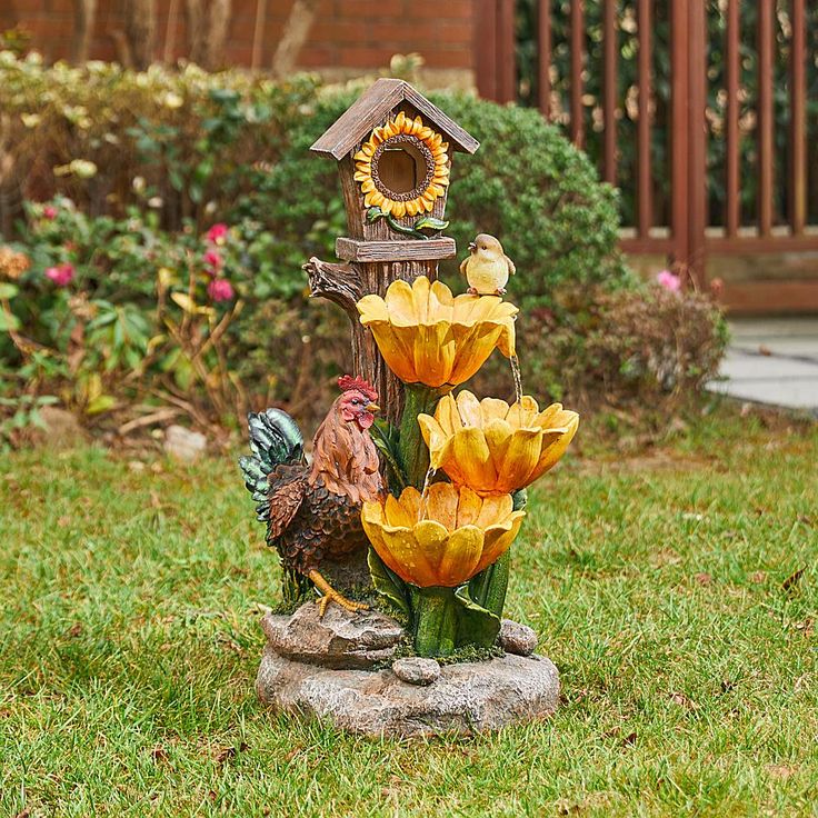 a birdhouse and flowers are in the yard with a rooster statue next to it