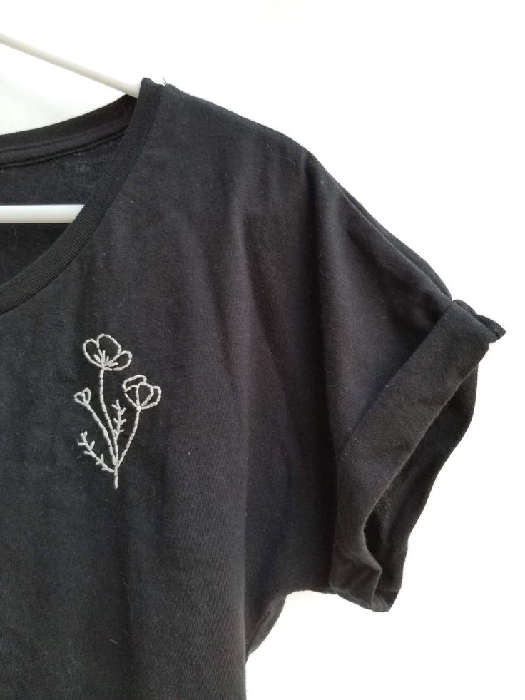 a black t - shirt with white flowers embroidered on the front and back, sitting on a hanger