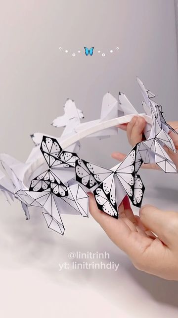 two hands holding origami butterflies in front of a white wall and butterfly background