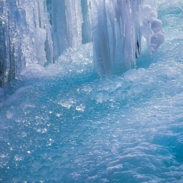 the water is crystal blue and there are ice formations hanging from the side of it