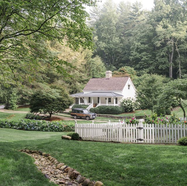 a white picket fence in front of a house with a car parked on the driveway