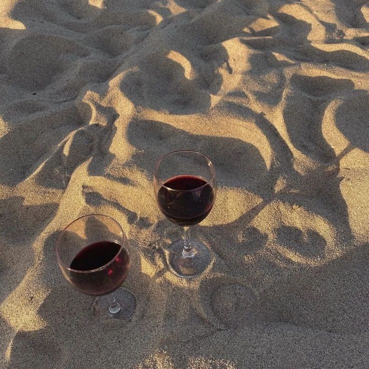 two glasses of wine sitting in the sand