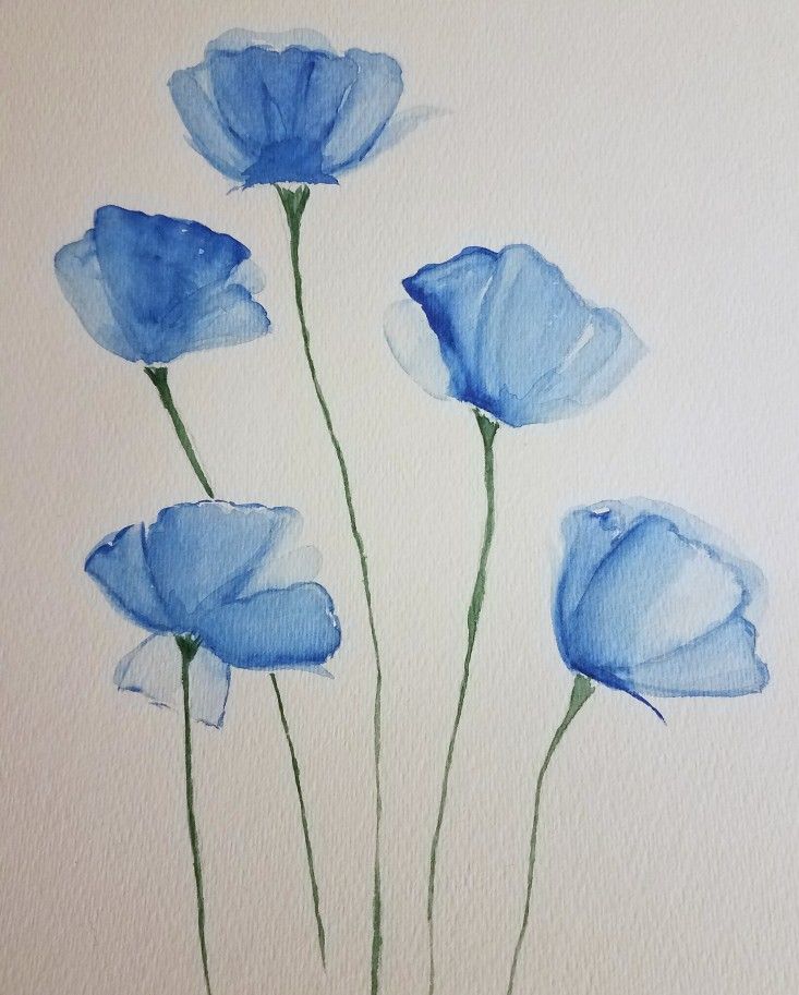 three blue flowers in a vase on a white surface with watercolor paper behind them