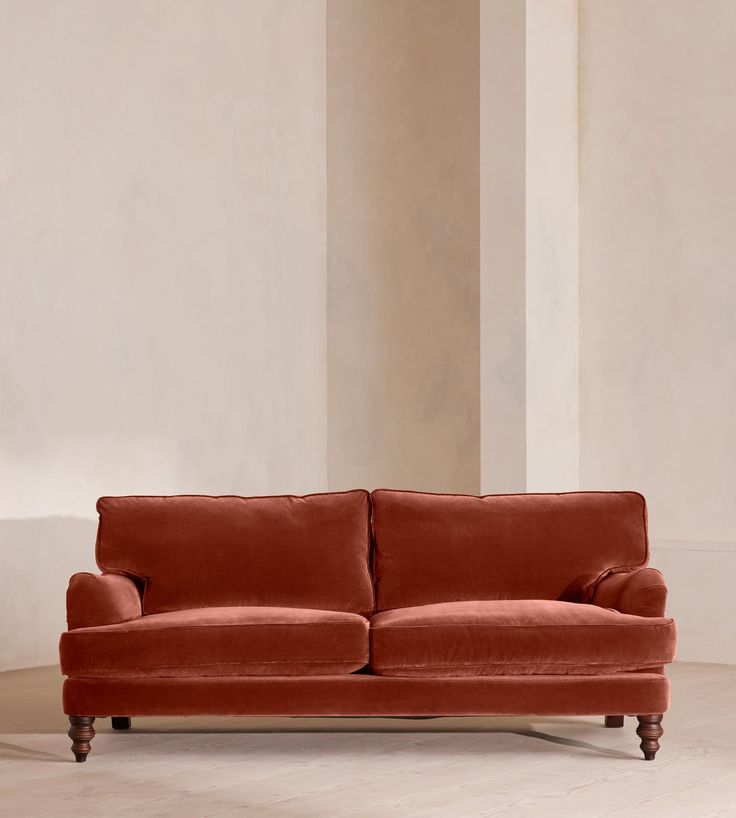 an orange couch sitting in a room next to a tall white wall and wooden legs