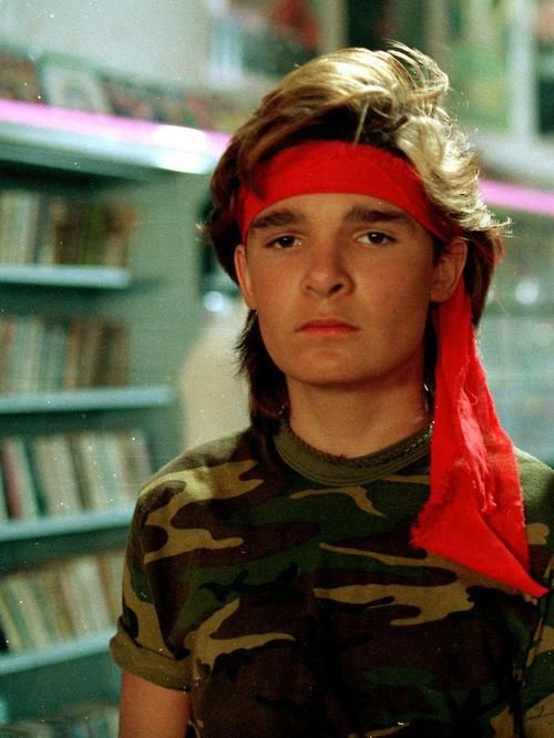 a young boy with a red bandana on his head in front of a bookshelf