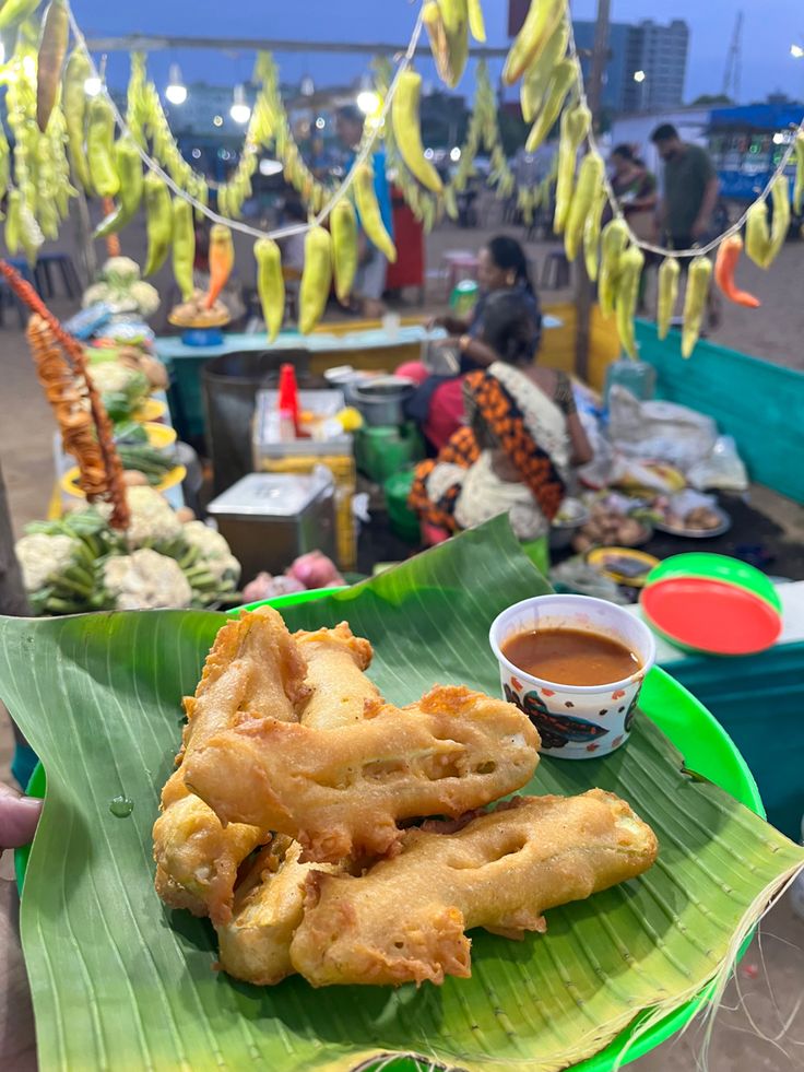 fried food on a banana leaf with dipping sauce in the middle and people standing around