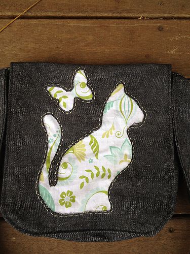 a small purse with a cat design on the front and back side, sitting on a wooden surface