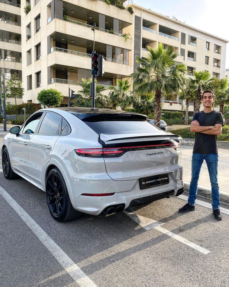 a man standing next to a white porsche cayenne