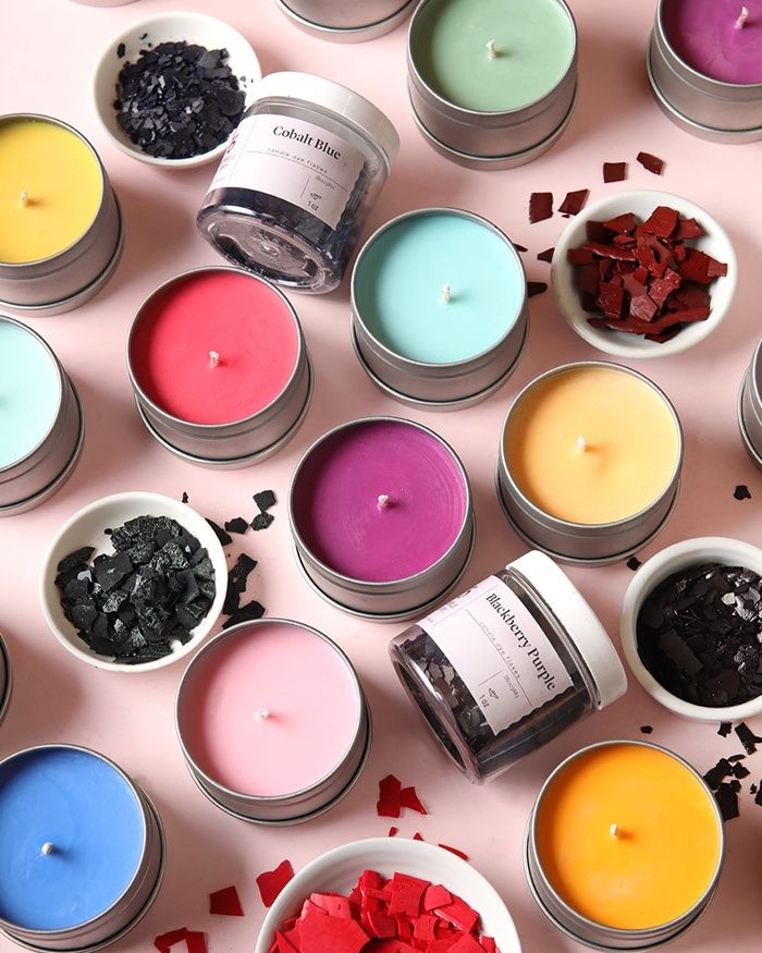 many different colored candles in small bowls on a pink surface with scattered confetti