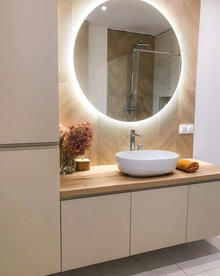 a bathroom with a round mirror above the sink and wooden countertop, along with white cabinets