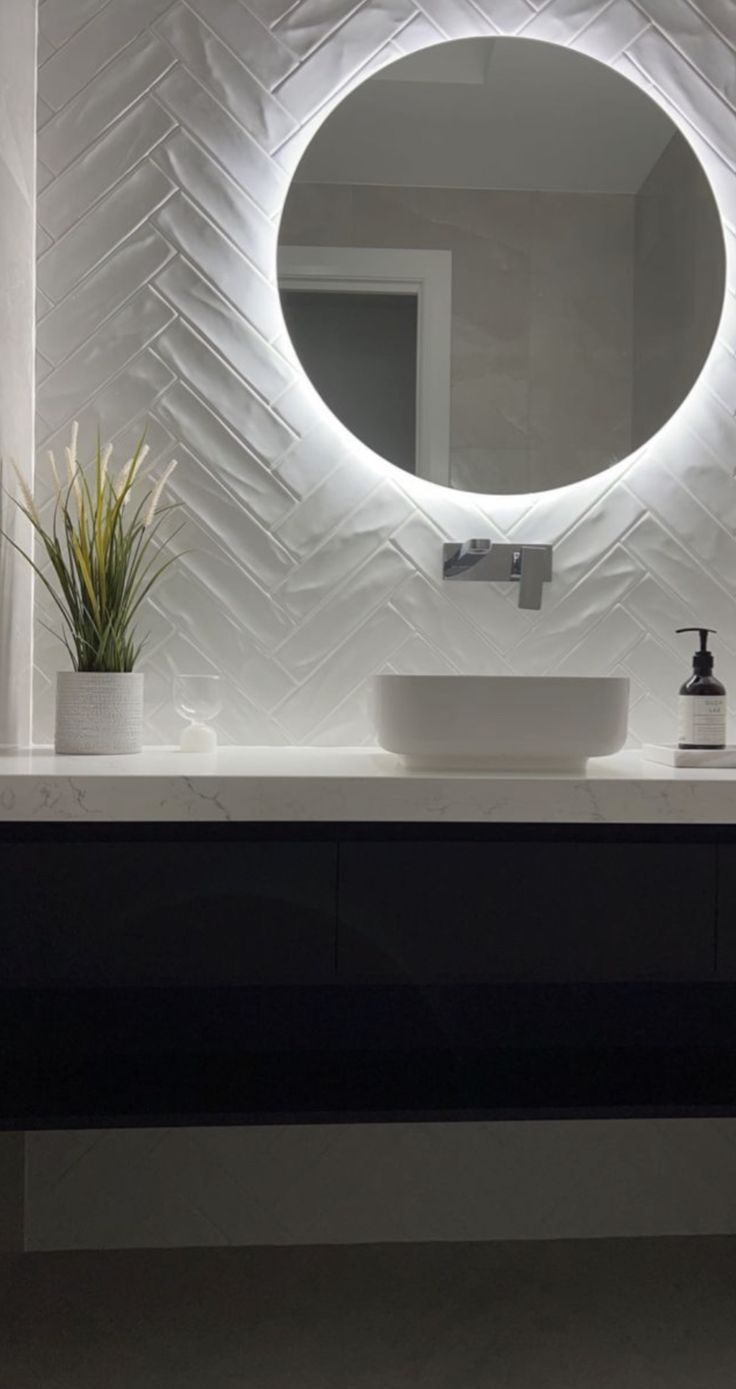 a bathroom sink with a round mirror above it and a potted plant on the counter