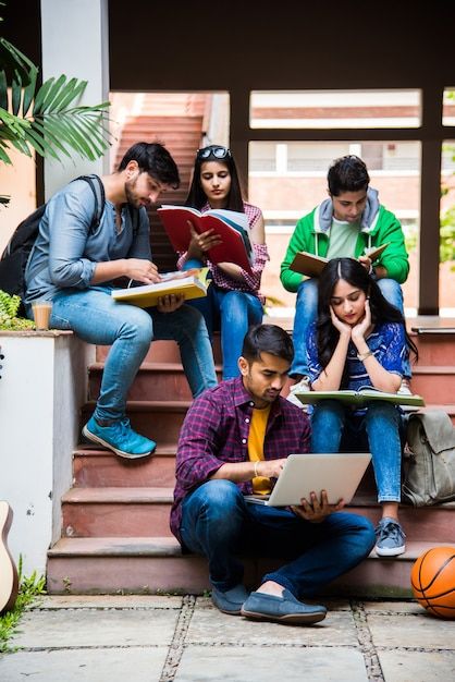 several people sitting on the steps with laptops and books in their hands while looking at something