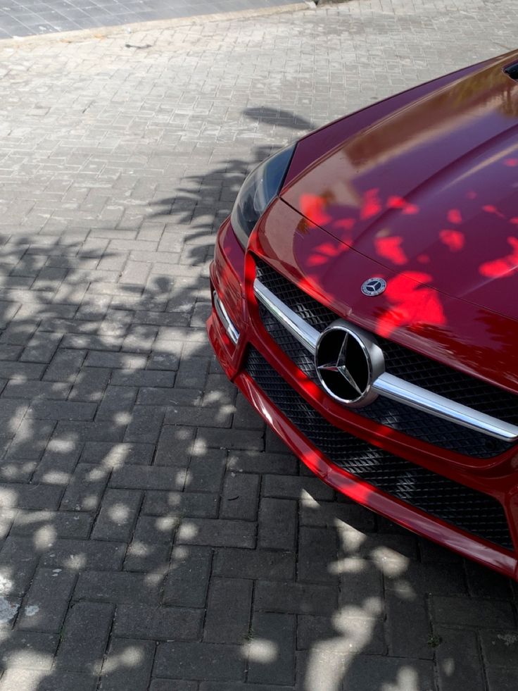 the front end of a red car parked on a brick sidewalk next to a tree