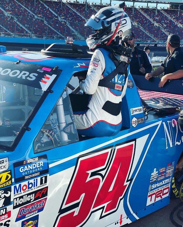 a man sitting in the back of a racing car at a race track with other people around him