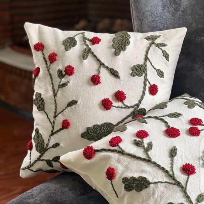 a white pillow with red flowers on it sitting on a gray chair in front of a fireplace