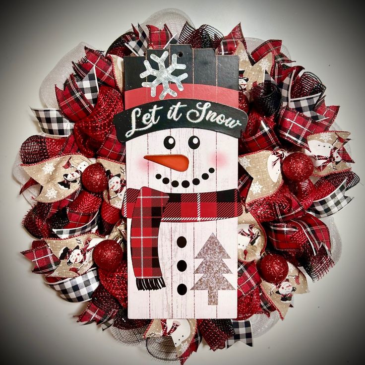 a christmas wreath with a snowman on the front and red plaid bow around it