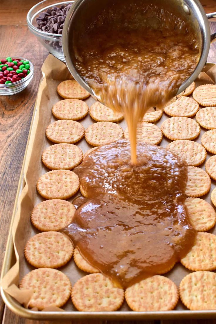 a person pouring caramel sauce on crackers in a baking pan with other snacks