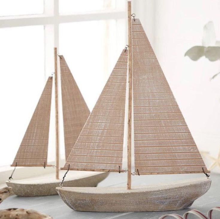 two wooden sailboats sitting next to each other on top of a table in front of a window