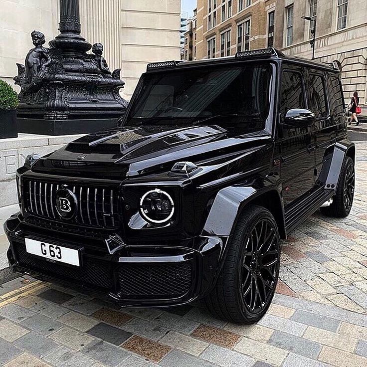 a black mercedes g - class parked on the street in front of a statue and building