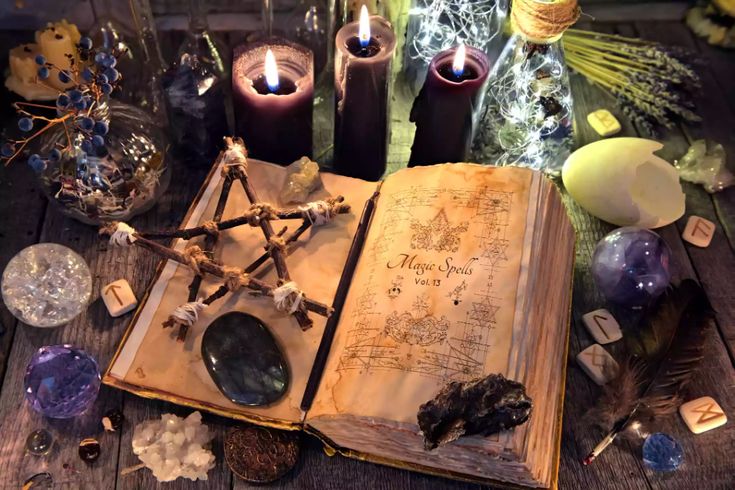 an open book sitting on top of a wooden table next to candles and other items