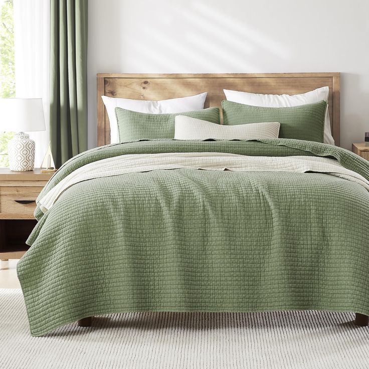 a bed with green bedspread and white pillows