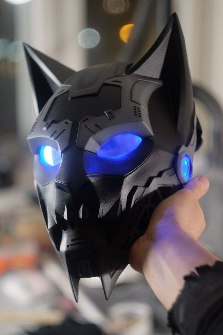 a hand holding a black cat mask with glowing blue lights on it's face