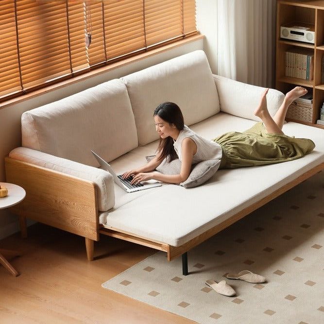 a woman laying on top of a white couch next to a table with a laptop