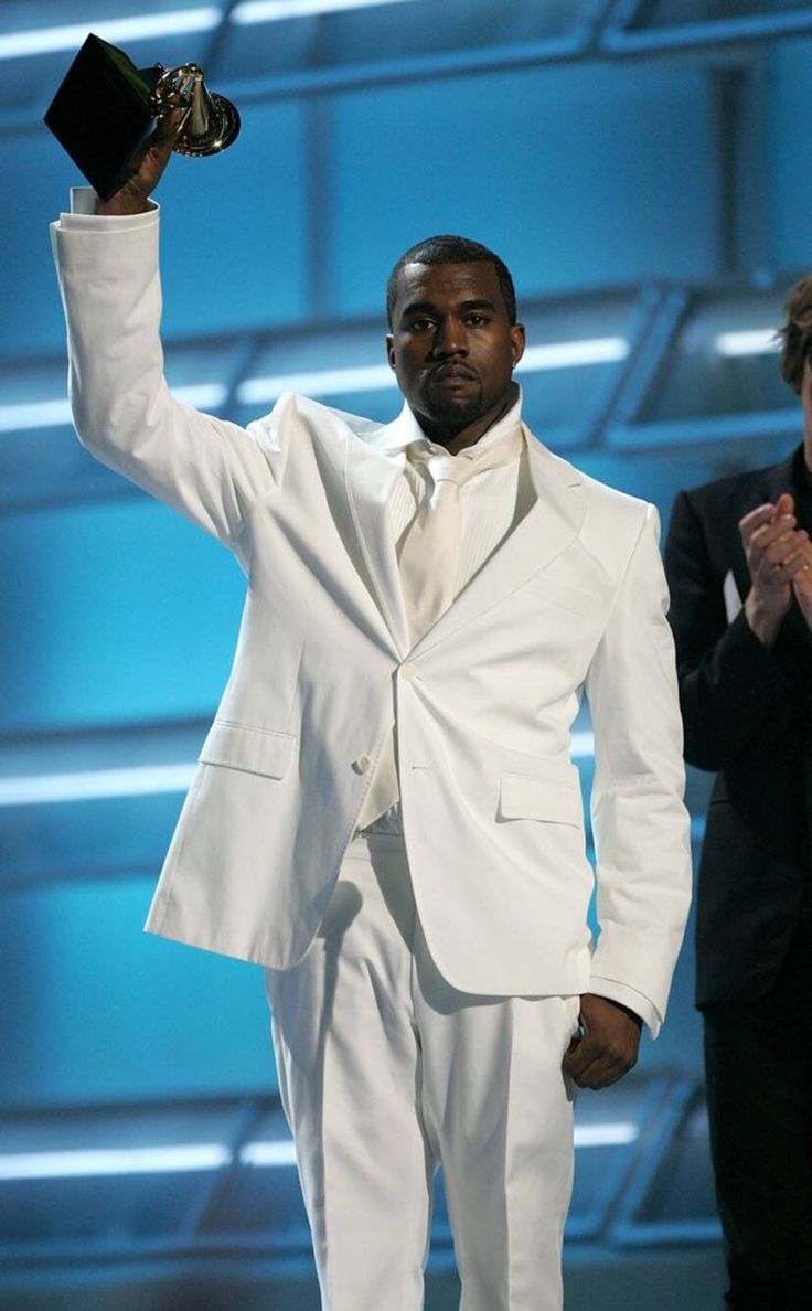 a man in a white suit and tie holding up an award while standing next to another man