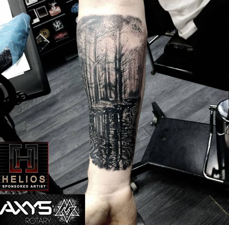 a person with a tattoo on their arm that has trees in the woods behind them