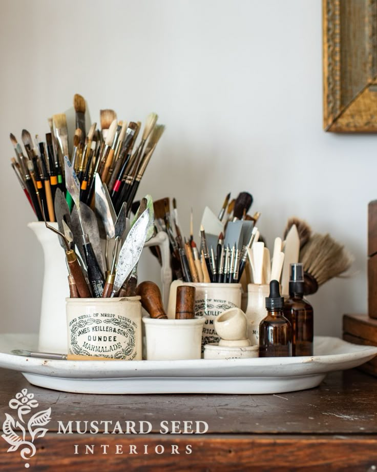 a white tray topped with lots of different types of paint and brushes on top of a wooden table