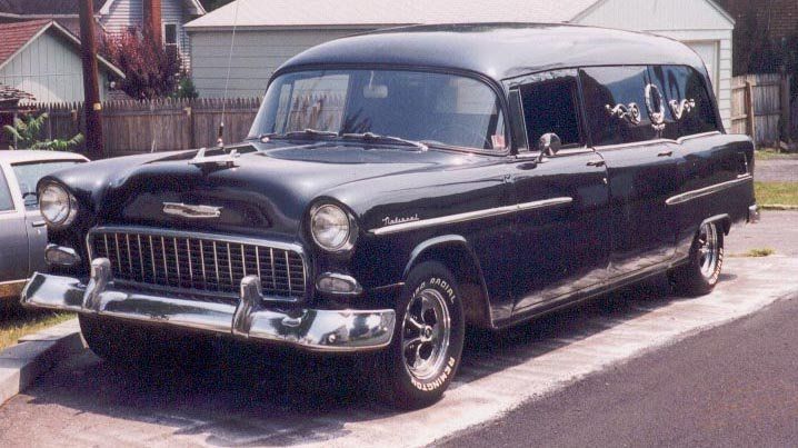 an old black car is parked on the side of the road in front of a house