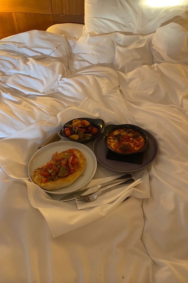 two plates of food on a bed with white sheets