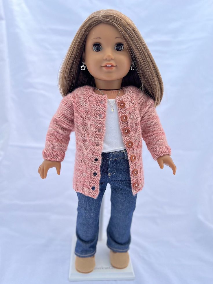 a doll is wearing a pink cardigan and jeans