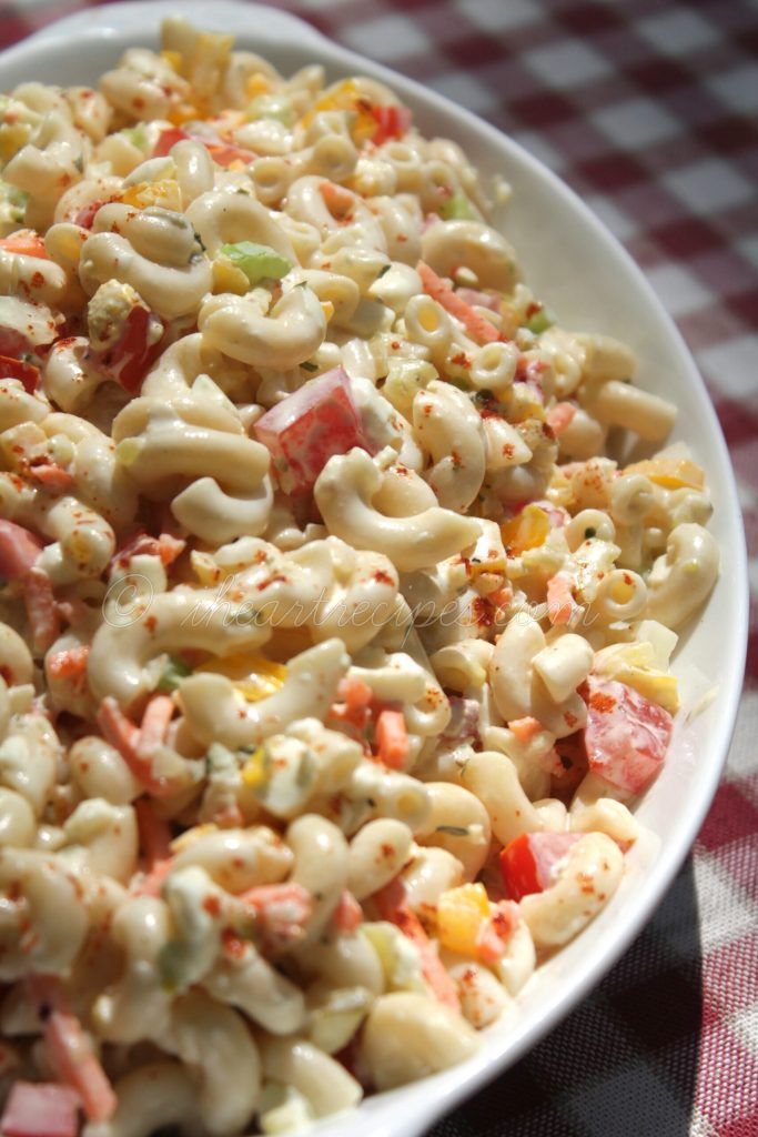 a white bowl filled with macaroni salad on top of a red and white checkered table cloth