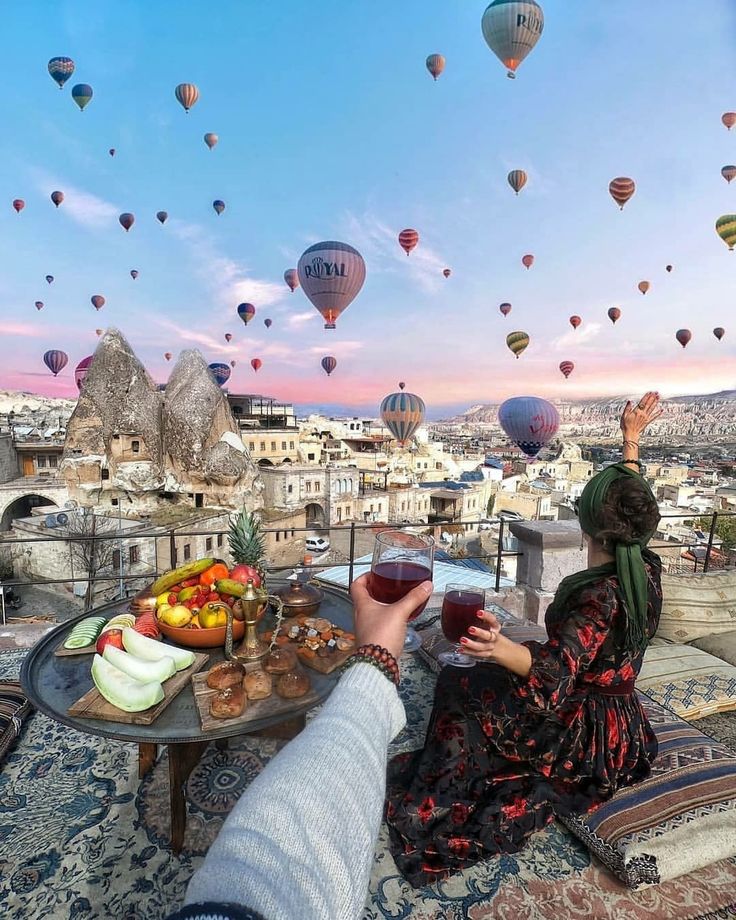 a woman sitting at a table with food and wine in front of hot air balloons