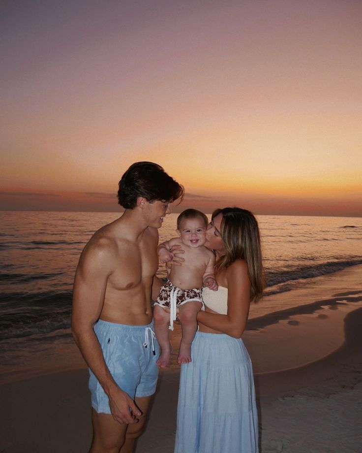 a man, woman and baby standing on the beach at sunset