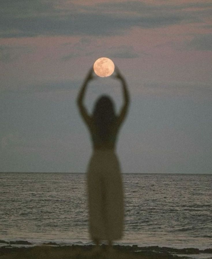 a woman standing on top of a beach next to the ocean holding a white frisbee