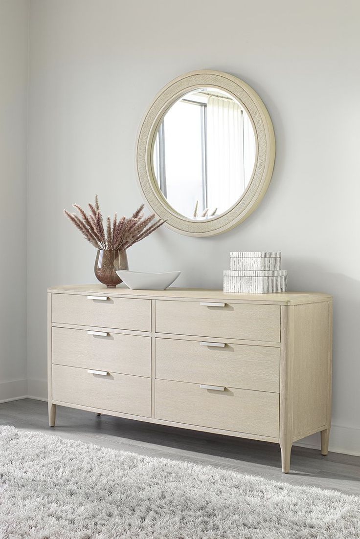 a white dresser with a round mirror on it's wall above it and a rug in front of it