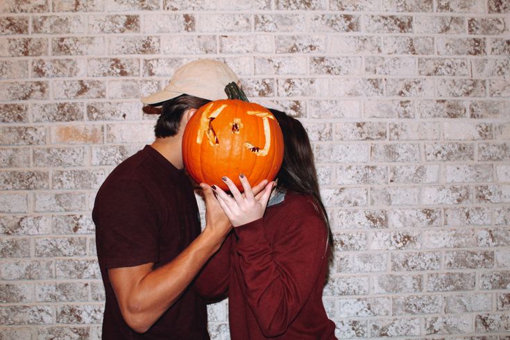 a man and woman holding up a pumpkin to their face