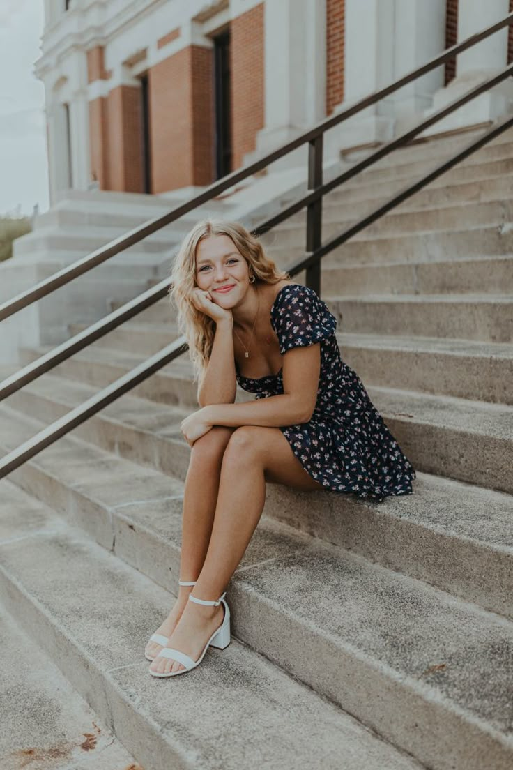 a woman sitting on the steps in front of a building with her hand under her chin