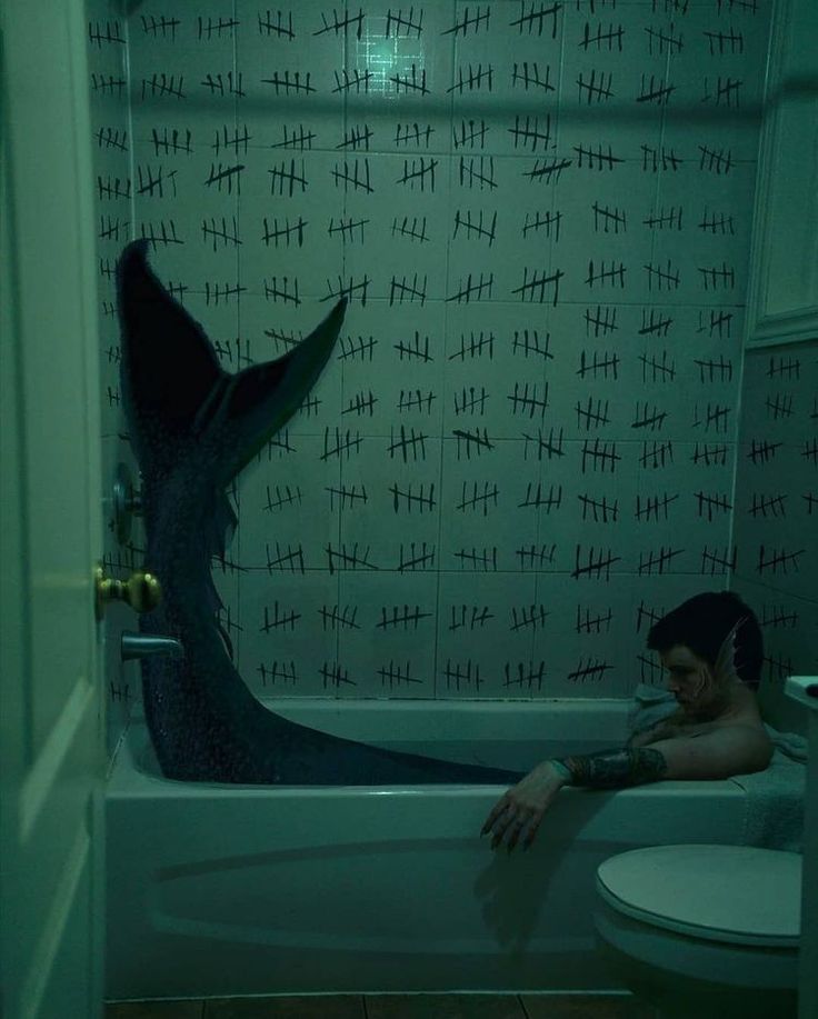 a man sitting in a bathtub next to a toilet under a shower curtain with black writing on it